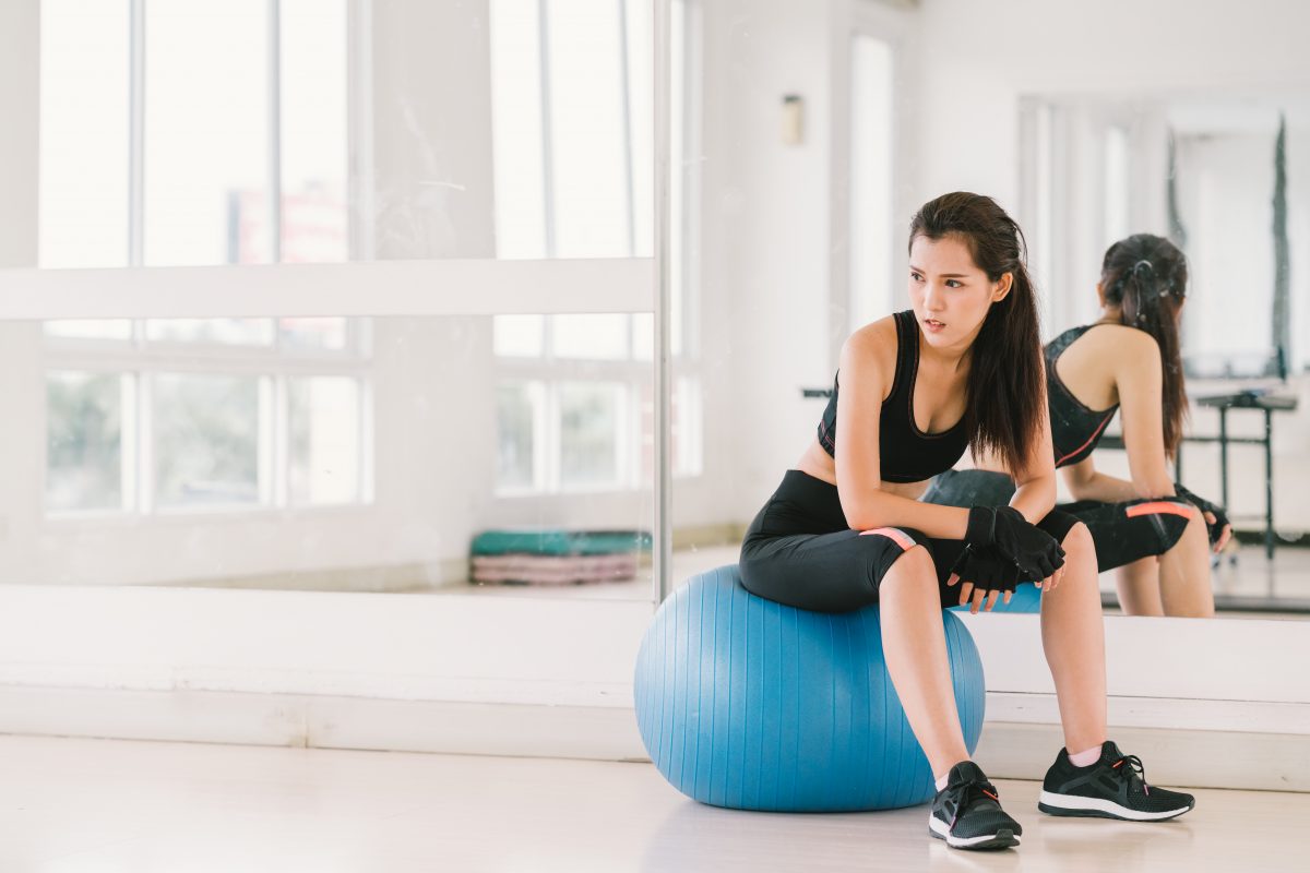 Young and determined sexy Asian girl on fitness ball at gym with copy space, sport and healthy lifestyle concept